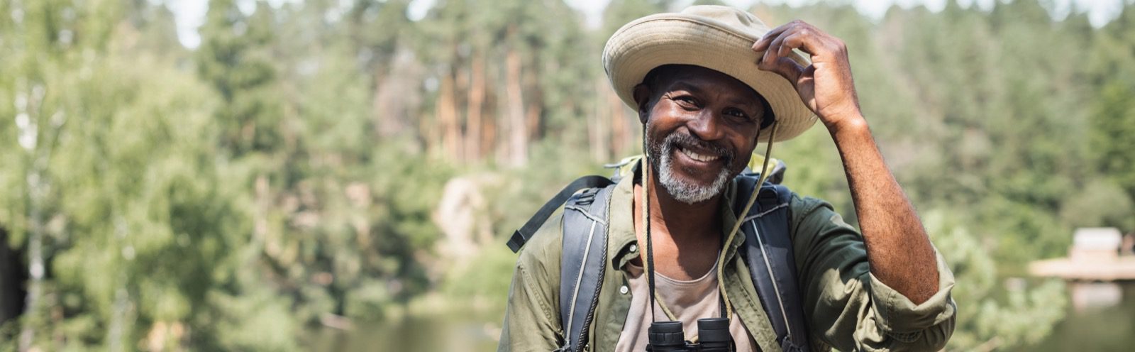 Smiling african american tourist with hat and binoculars looking at camera outdoors, banner,stock image